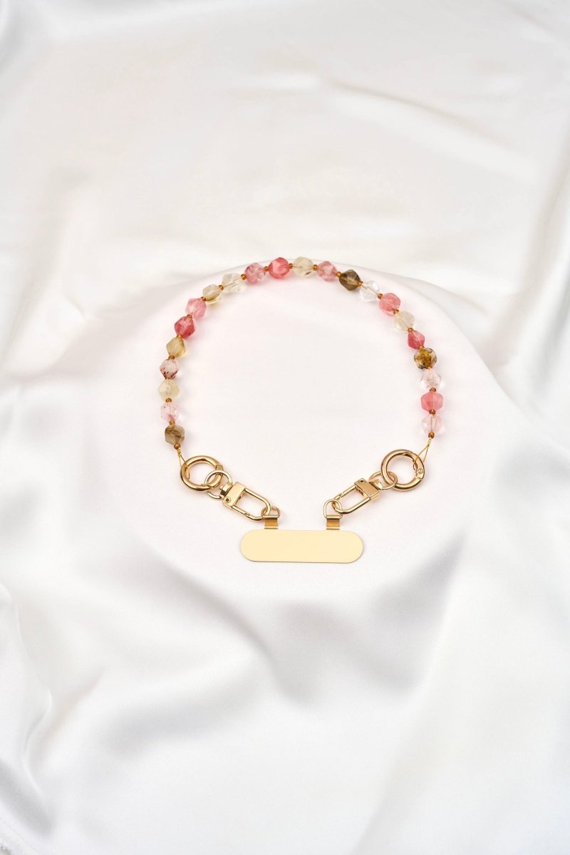 strap corto artesanal para celular con cuentas de cristal y broches dorados sobre fondo blanco.