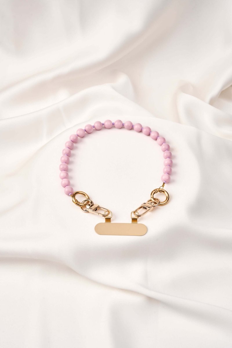 Strap celular artesanal Soft Aura en color rosa con broches dorados sobre un fondo blanco.