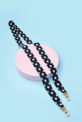 strap polka luxe negro artesanal sobre fondo azul con soporte redondo rosa.