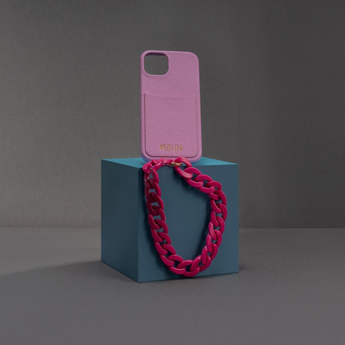 Cadena de lujo para celular y funda de cuero en fucsia sobre pedestal azul, elegante y moderno.