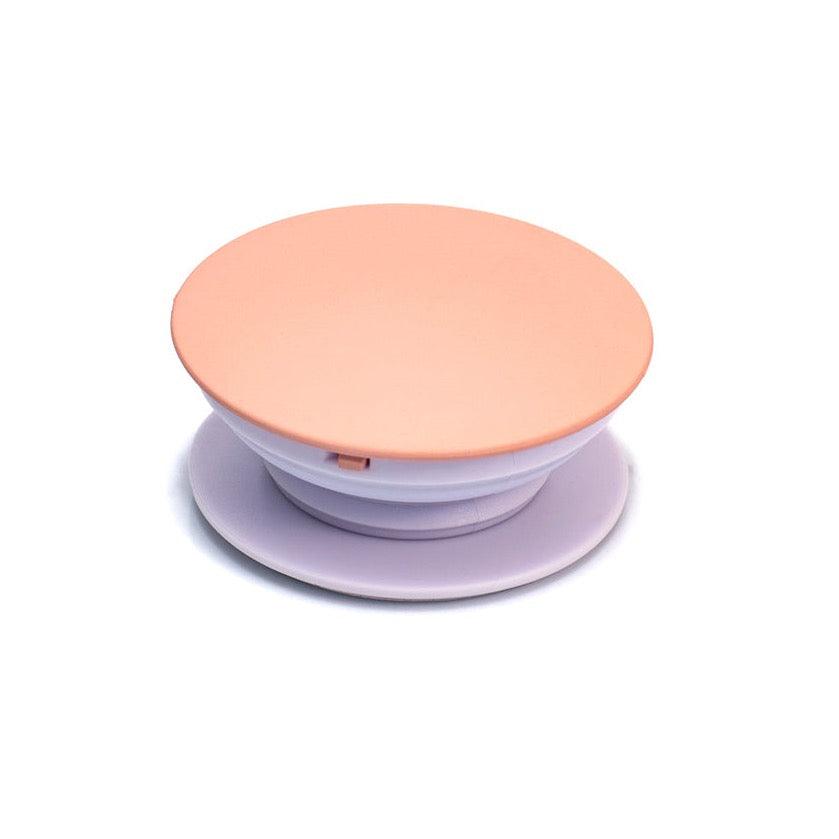 Soporte para celular Malak con sistema adhesivo, diseño circular en color melocotón y lila.